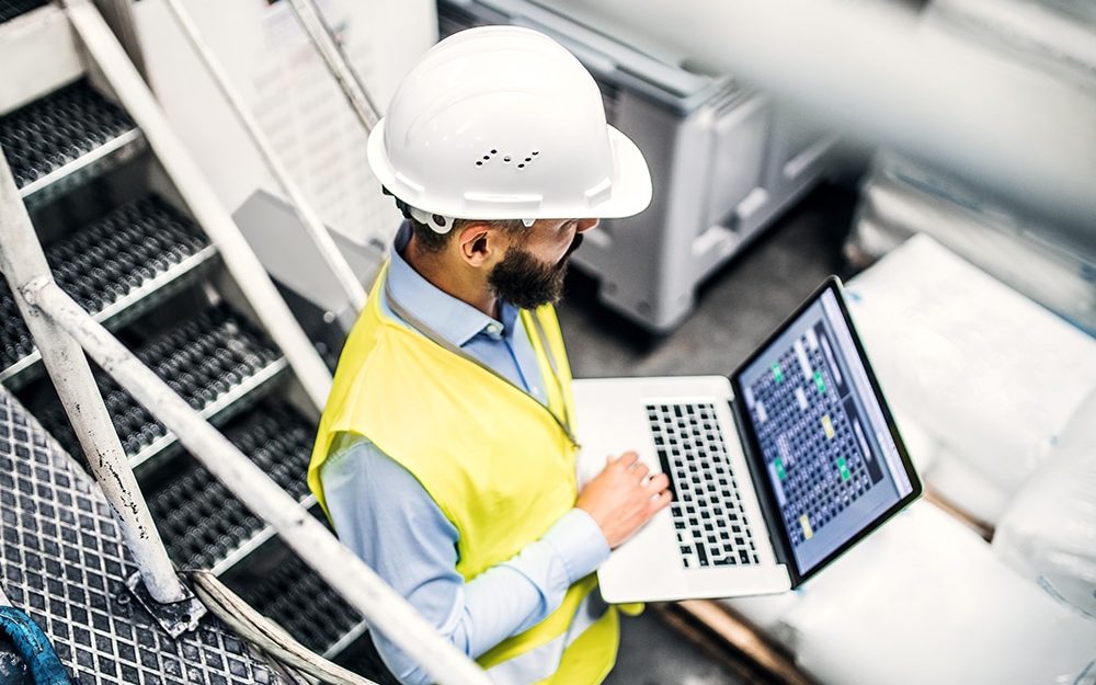 Ingeniero con laptop revisando equipo desde una pasarela de la planta